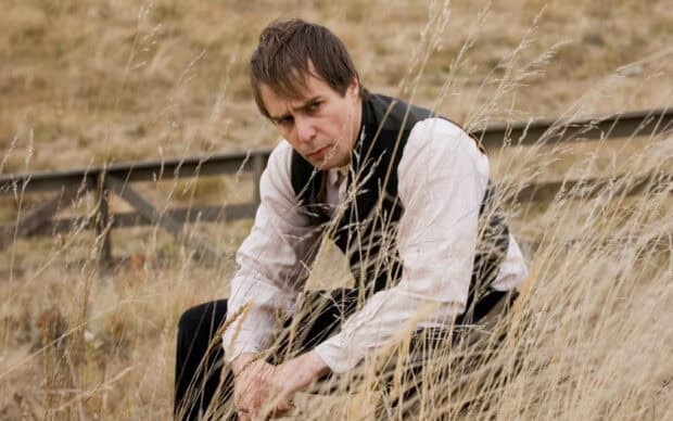 Sam Rockwell is sitting in a dry field with tall grass looking serious, 2K Desktop Wallpaper