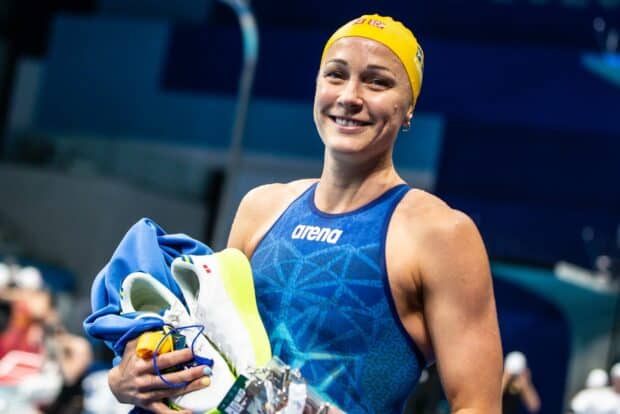 Sarah Sjostrom smiles holding shoes and towel at a swimming event, HD Desktop Wallpaper