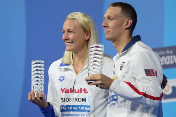Sarah Sjostrom is smiling while holding a trophy with another athlete at a sports event, 2K Desktop Wallpaper