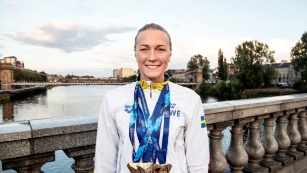 Sarah Sjostrom proudly poses with her medals outdoors near a river, HD Desktop Wallpaper
