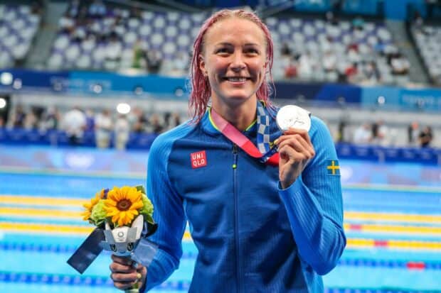 Sarah Sjostrom smiles while holding a silver medal and flowers at a swimming event, HD Desktop Wallpaper