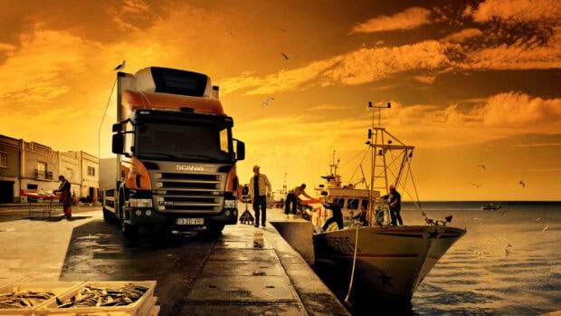 A Scania truck is parked at a harbor with fishermen working nearby during sunset, HD Desktop Wallpaper