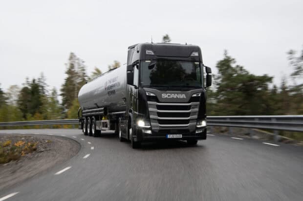 A black Scania truck is driving along a forested curved road, 2K Desktop Wallpaper