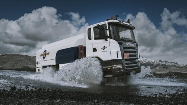 A Scania truck is driving through a shallow body of water with mountains in the background, HD Desktop Wallpaper