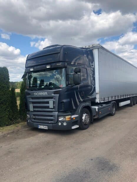 A black Scania truck parked on a country road with a cloudy sky reflected on the windshield, 2K Desktop Wallpaper