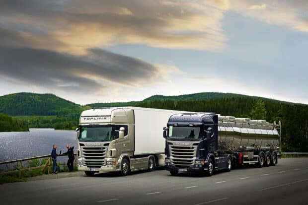 Two Scania trucks parked by a lakeside road with forested hills in the background, HD Desktop Wallpaper