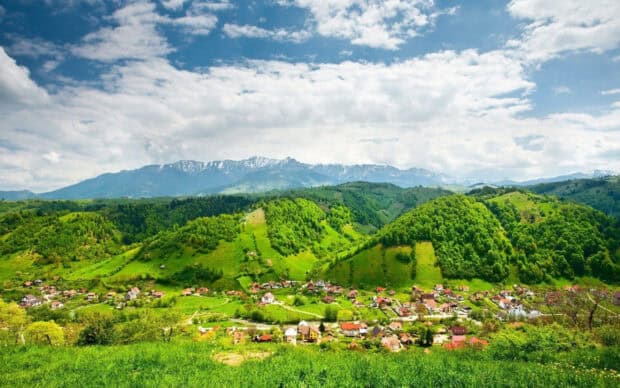 A peaceful village sits among green hills under a cloudy blue sky featuring village wallpapers, 2K Desktop Wallpaper