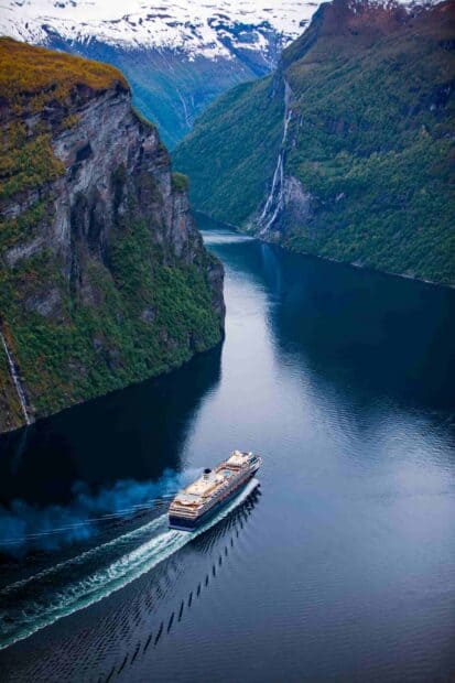 A ferry navigates a calm fjord surrounded by steep cliffs and snow capped mountains, 2K Mobile Wallpaper