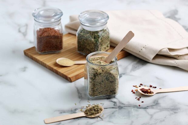 A glass jar filled with seasoning shows various herbs and spices on spoons, 2K Desktop Wallpaper