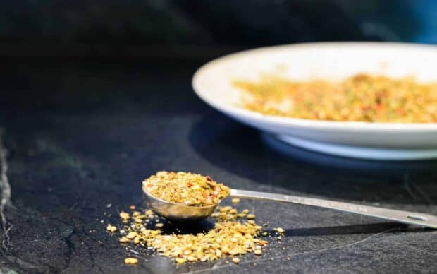 A metal spoon holds a mix of seasoning with some spilled on a dark surface, HD Desktop Wallpaper