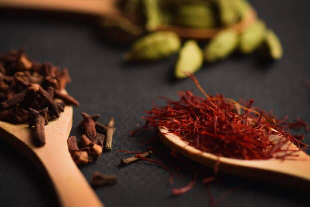 A close up of seasoning with saffron, cloves, and cardamom on wooden spoons, 2K Desktop Wallpaper