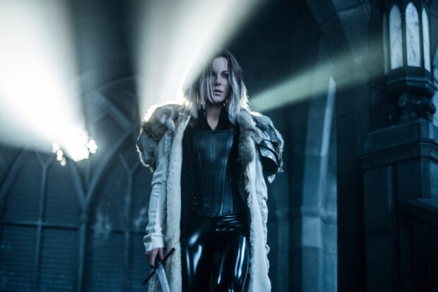 Selene stands in a gothic hall wearing black and white fur with a sword, 2K Desktop Wallpaper