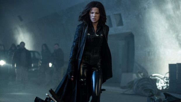 Selene in a dark leather outfit walking in an underground setting with people behind her, 4K Desktop Wallpaper