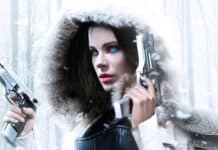 A fierce woman with blue eyes holding two guns in a snowy forest scene of Selene Underworld, 2K Desktop Wallpaper