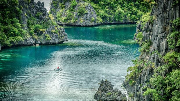 A small boat sails along the clear Palawan waters surrounded by lush cliffs, HD Desktop Wallpaper