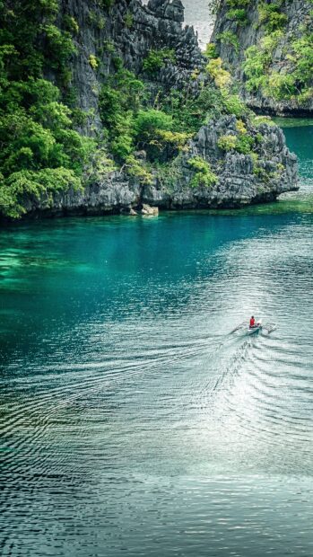 A person rows a boat through clear blue water surrounded by rocky cliffs in Palawan wallpapers, HD Mobile Wallpaper