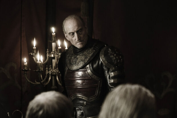 A man wearing detailed armor stands near lit candles in a dim room, HD Desktop Wallpaper