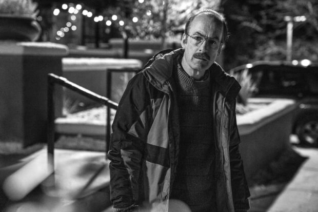 Bob Odenkirk stands outdoors wearing a jacket and glasses in a nighttime setting, HD Desktop Wallpaper