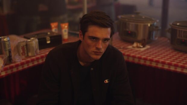 A young man wearing a dark jacket sits at a table with kitchenware behind him, HD Desktop Wallpaper