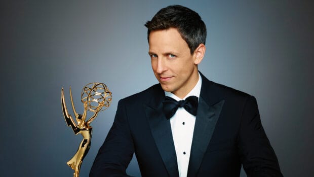 Seth Meyers poses confidently holding an Emmy Awards trophy in a black tuxedo, HD Desktop Wallpaper