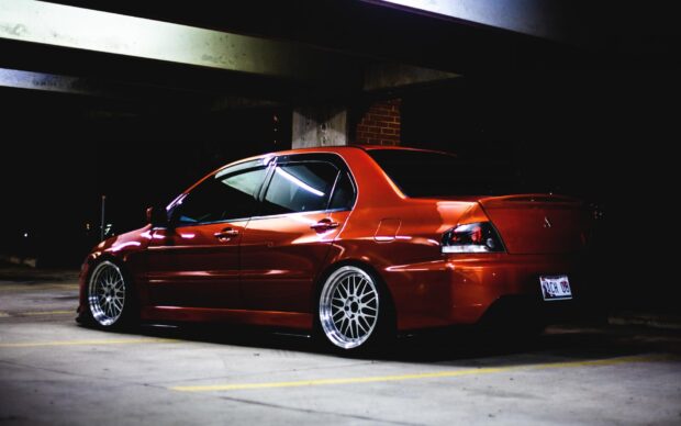 A red Lancer Evo car is parked inside a dimly lit garage at night, HD Desktop Wallpaper