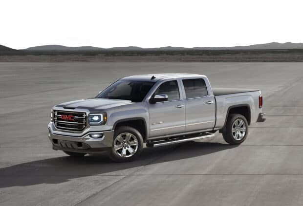 A silver GMC Sierra truck is parked on a vast concrete area with mountains in the distance, 2K Desktop Wallpaper