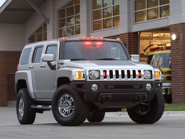 A silver Hummer H3 is parked on the street near a brick building with large windows and a fire truck in the background, HD Desktop Wallpaper