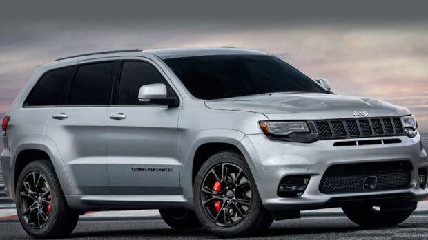 A silver Jeep Grand Cherokee is parked under a cloudy sky showing its black wheels and red brake calipers, 4K Desktop Wallpaper