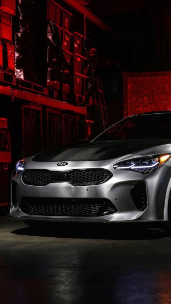 A silver Kia Stinger is parked in a dimly lit garage with red ambient lighting and visible storage boxes, 4K Mobile Wallpaper
