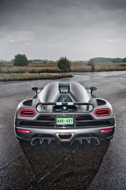 A silver Koenigsegg is parked on a wet road under a cloudy sky with trees in the background, HD Phone Wallpaper
