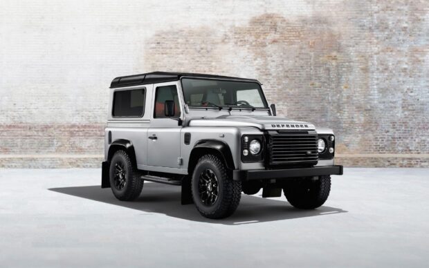 A silver Land Rover Defender is parked indoors with a textured brick wall in the background, 2K Desktop Wallpaper