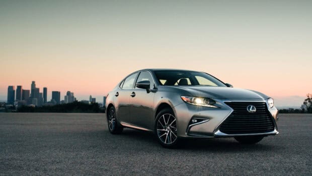A silver Lexus ES is parked on an open road with a city skyline visible during sunset, 4K Desktop Wallpaper