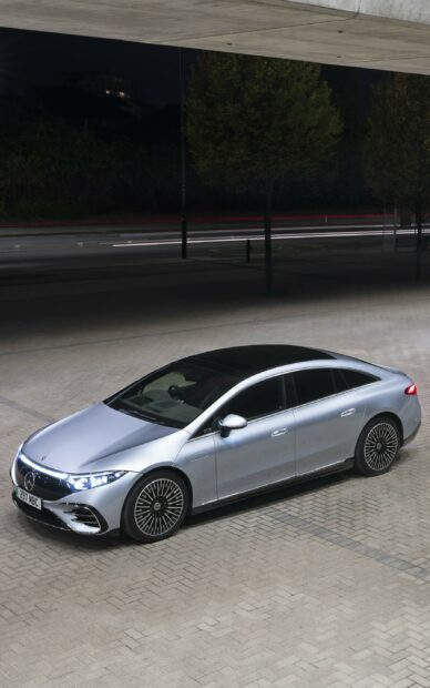 Silver Mercedes Benz EQS is shown parked on a paved area at night with illuminated headlights, 2K Phone Wallpaper