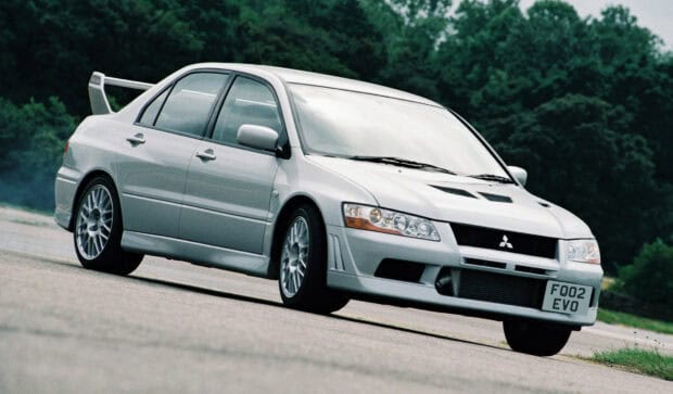 A silver Mitsubishi Lancer Evo is captured driving on a clear asphalt road with green trees in the background, HD Desktop Wallpaper