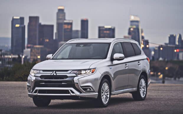 A silver Mitsubishi Outlander is parked on an urban road with skyscrapers in the background, 2K Desktop Wallpaper