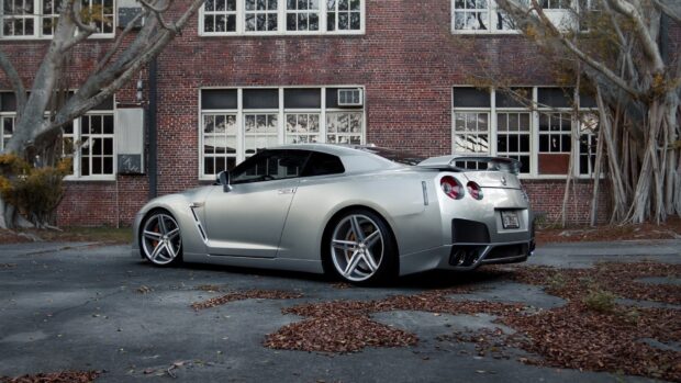 A silver Nissan GT R is parked on the pavement near an old brick building with large windows, HD Desktop Wallpaper