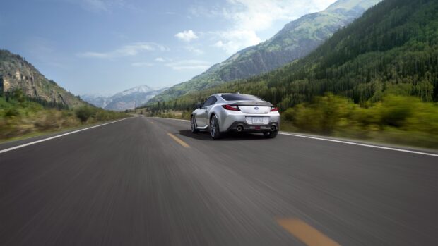 A silver Subaru Brz is driving fast on a scenic mountain road surrounded by green forests and hills, HD Desktop Wallpaper