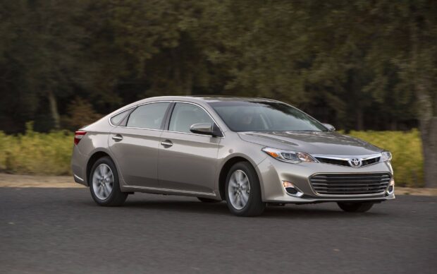 A silver Toyota Avalon drives smoothly on a paved road near green trees, 2K Desktop Wallpaper