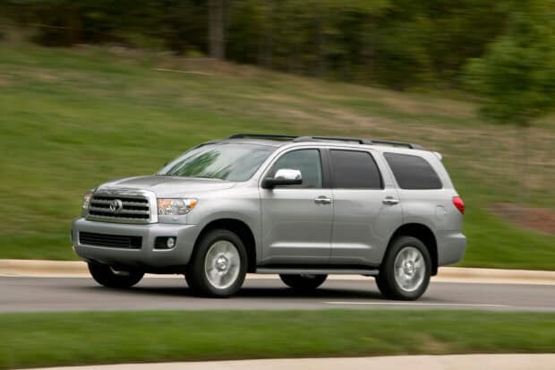 A silver Toyota Sequoia is driving on a suburban road with greenery in the background, 2K Desktop Wallpaper