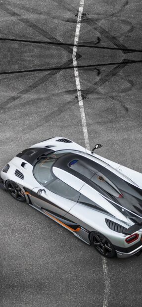 A sleek silver and black Koenigsegg is parked on an asphalt surface with tire marks, 2K Phone Wallpaper