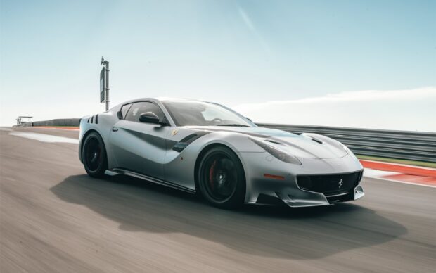 A silver sports car speeds along a race track under a clear blue sky showcasing power and design, 2K Desktop Wallpaper