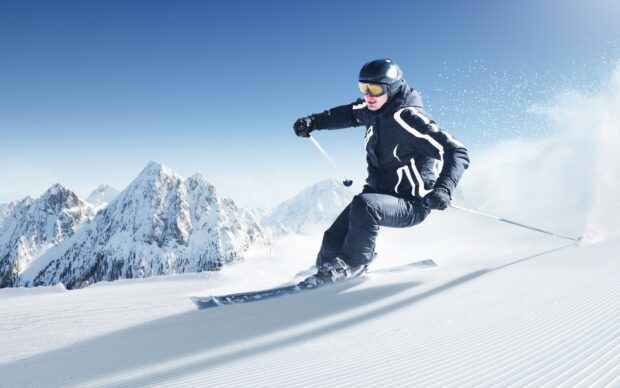 A skier is carving through fresh snow with mountain peaks in the background, HD Desktop Wallpaper