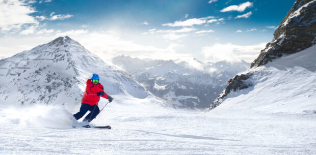 A skier in red outfit skiing down a snowy mountain under a blue sky, HD Desktop Wallpaper