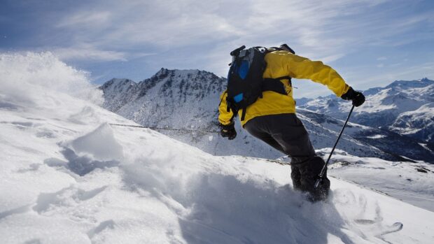 A skier in a yellow jacket is skiing down a snowy mountain slope with clear skies, HD Desktop Wallpaper