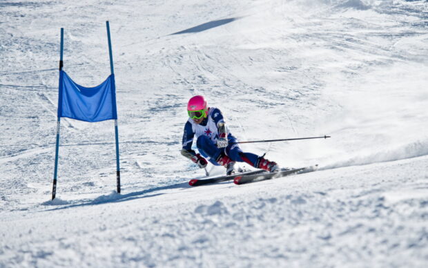 A skier wearing a pink helmet moves swiftly past a blue gate in a skiing competition, 2K Desktop Wallpaper