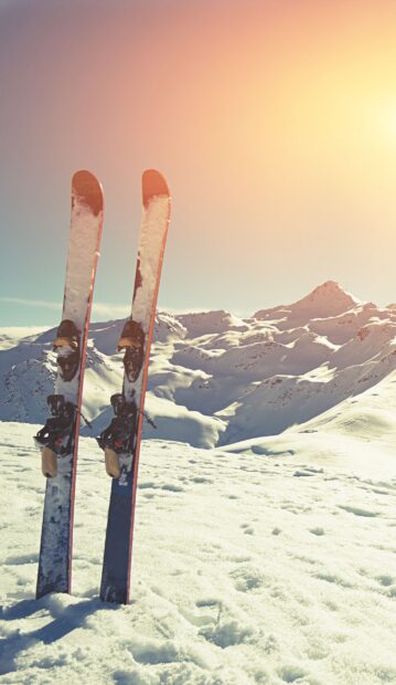 A pair of skis standing in fresh snow with mountain peaks in the sunlit background featuring skiing wallpapers, 2K Mobile Wallpaper