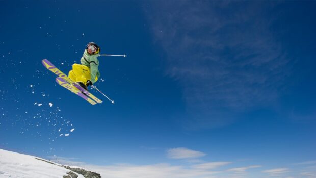 A skier performs a high jump against a clear blue sky in the mountains, HD Desktop Wallpaper