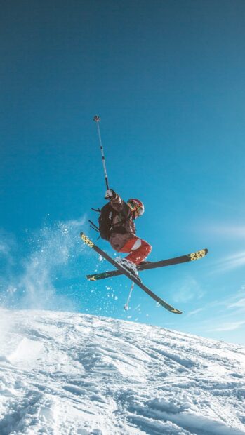A skier performs an impressive jump over snowy terrain with bright blue sky, 2K Phone Wallpaper