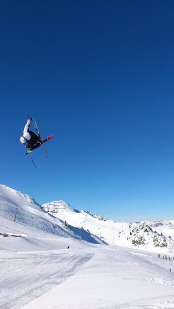 A skier performs a high jump in the snowy mountains under a clear blue sky with skiing wallpapers, 2K Mobile Wallpaper