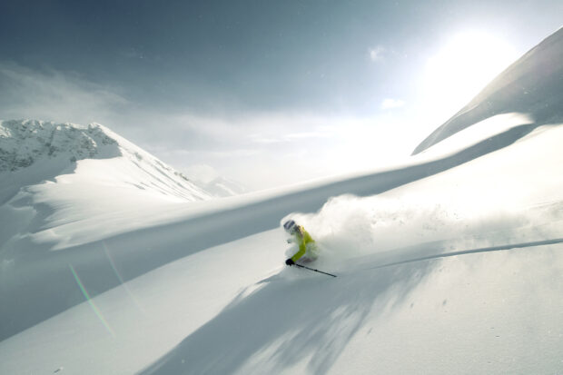 A skier wearing a yellow jacket skiing downhill through fresh snow on a sunny day, HD Desktop Wallpaper